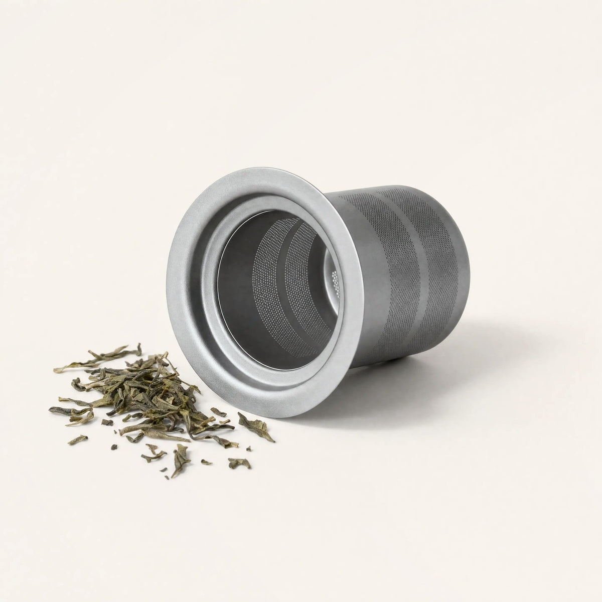 Titanium tea filter on its side with loose green tea leaves